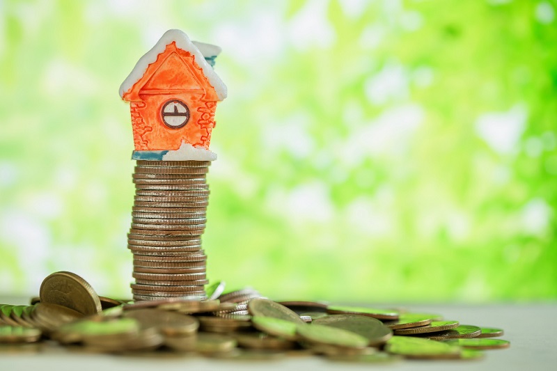 Mini house on stack of coins with green background.